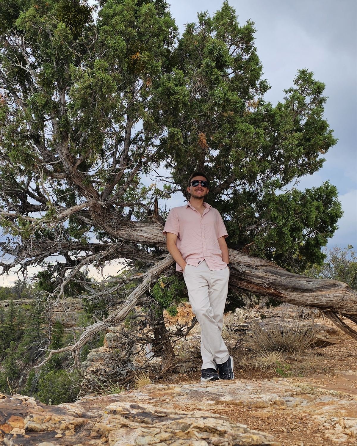 Bogdan Gerasymenko leaning against a juniper tree on a canyon rim
